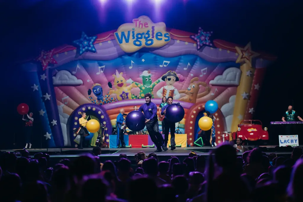 The Wiggles group plays with large colorful bouncing balls on stage.
