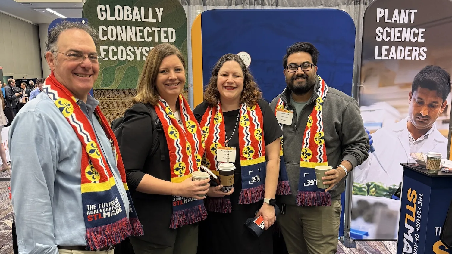 People in the agtech industry wearing St. Louis flag scarves stand in front of an STL-Made booth.