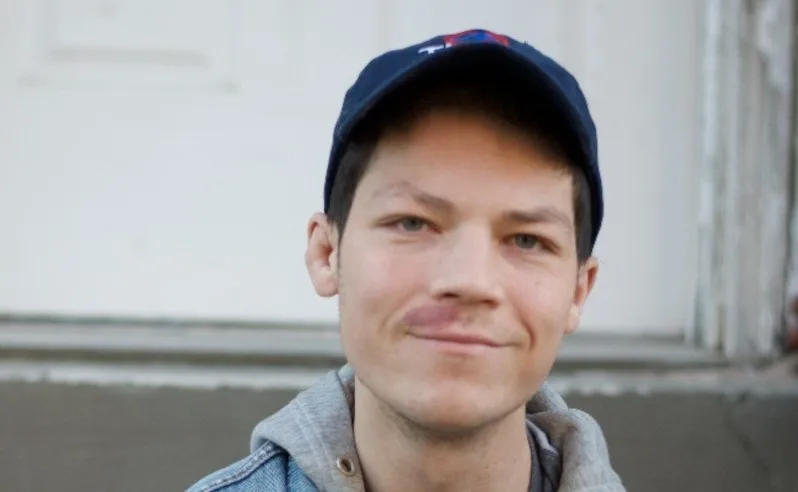 A young man wearing a ballcap looks at the camera.