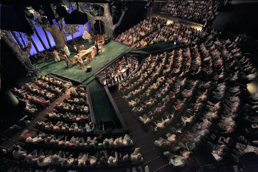 A full audience capturing a live performance at the Opera Theatre of Saint Louis accompanied by a live orchestra.