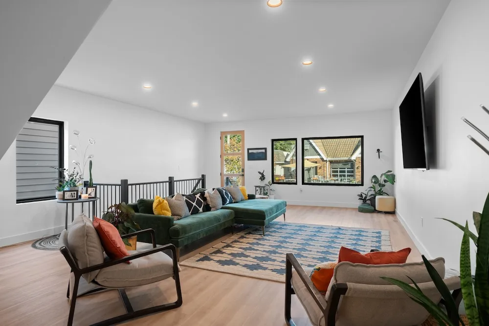 Bright open-concept living room by Campbell House and Home with a green sectional and mid-century accents.