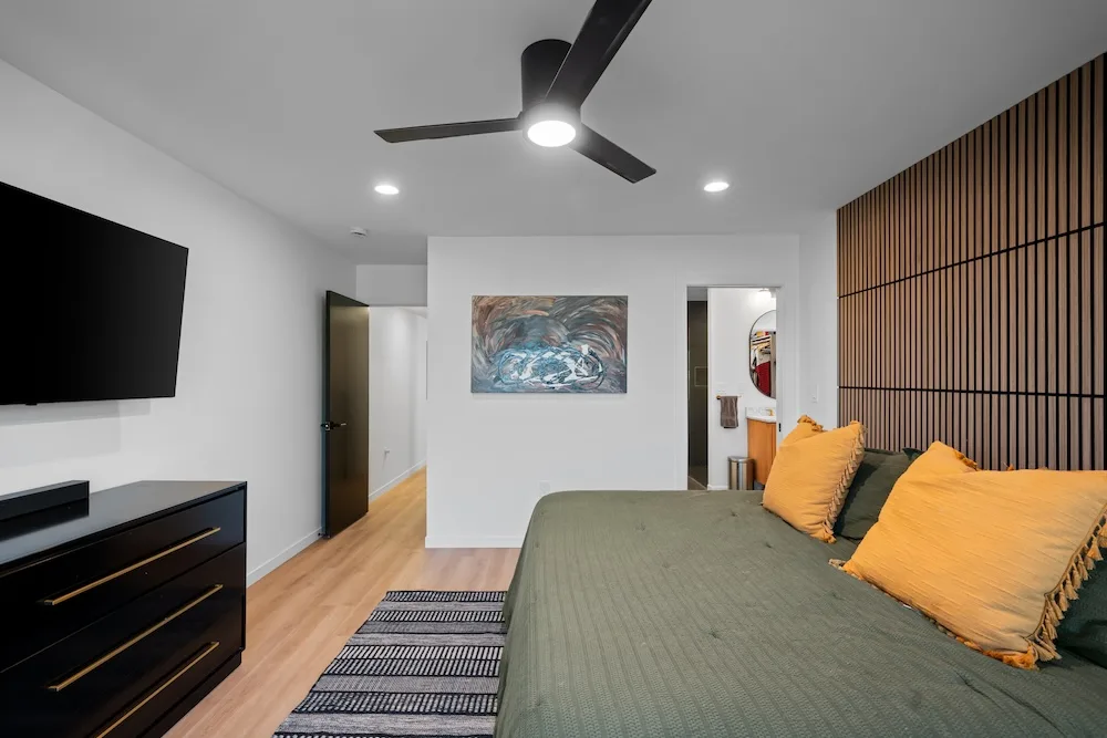 Primary bedroom designed by Campbell House and Home featuring a slatted wood accent wall and warm color palette.