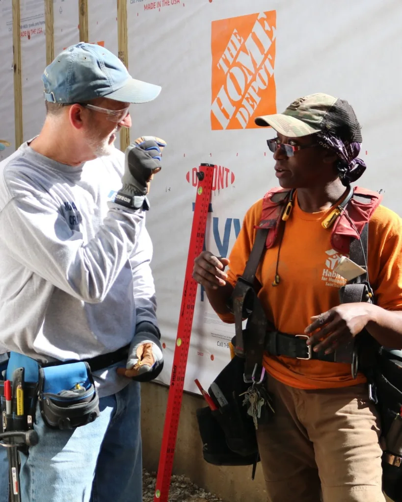 Two Habitat for Humanity Saint Louis volunteers wearing tool belts and working together at a construction site.