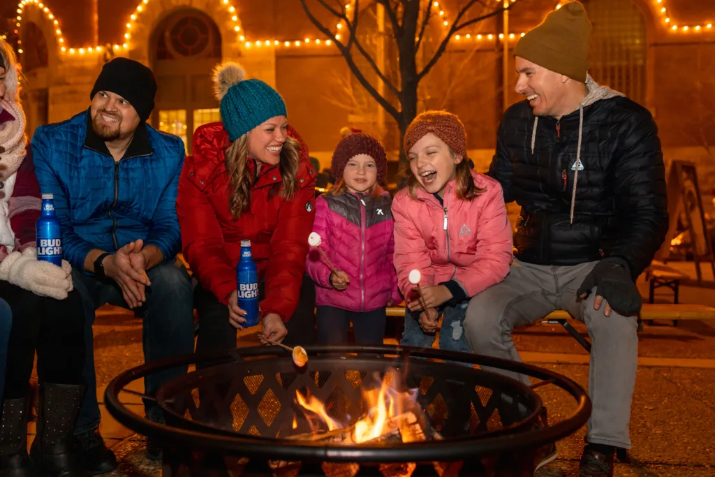 A family sitting around a fire pit roasting marshmallows during Brewery Lights.