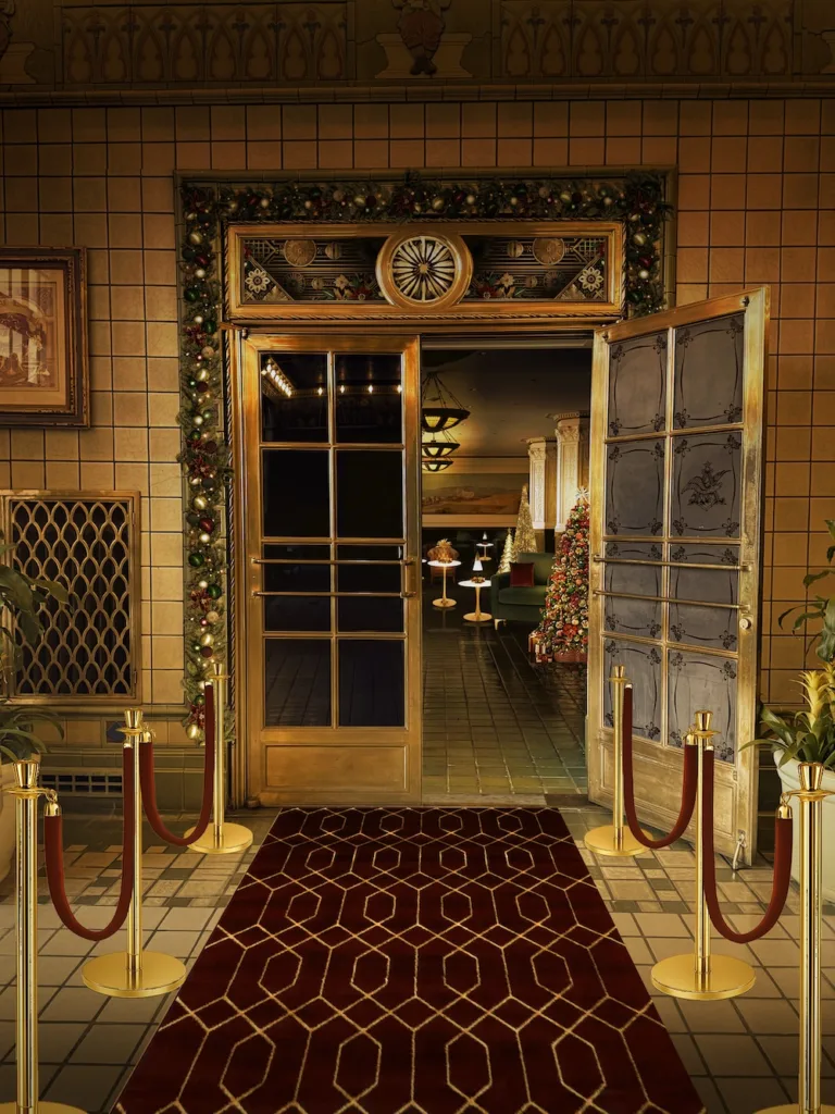 A warmly lit speakeasy-style entrance decorated with garlands, gold accents, and a red carpet leading into a holiday-themed lounge.