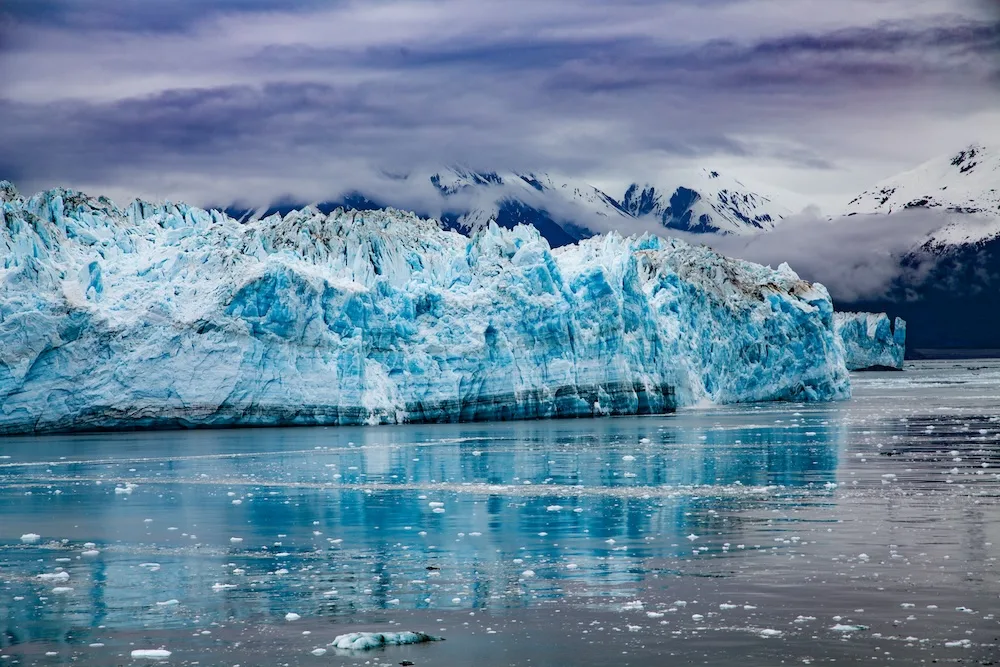 Hubbard Glacier rises from icy waters under dark storm clouds in Alaska.