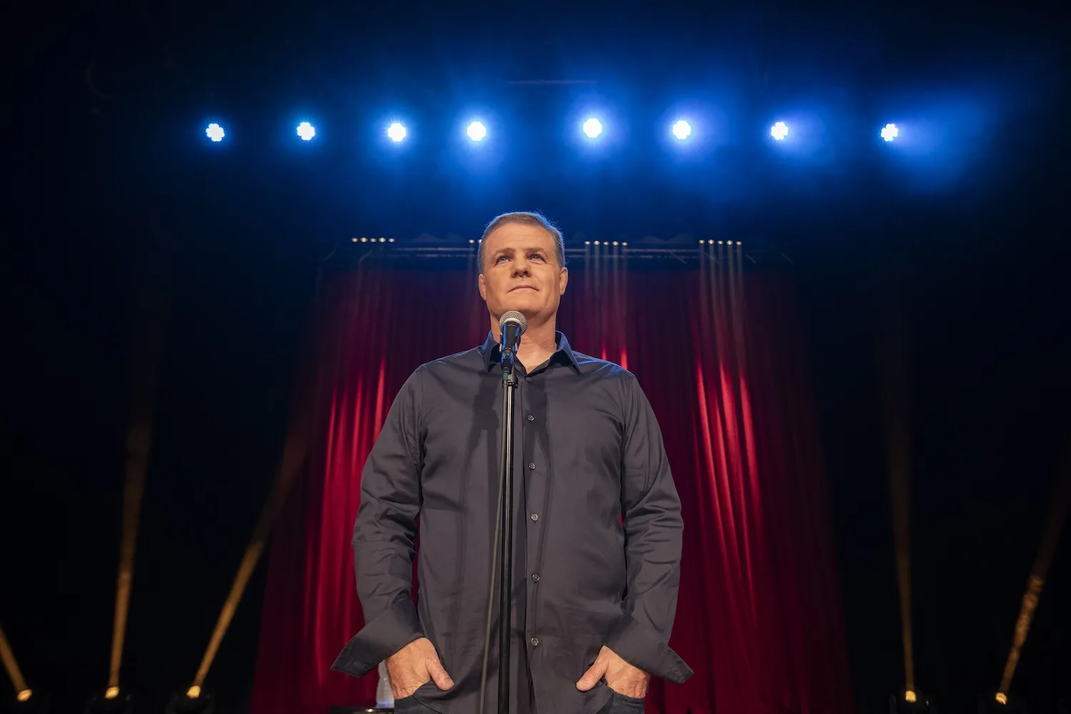A man stands on stage with blue lights behind him.