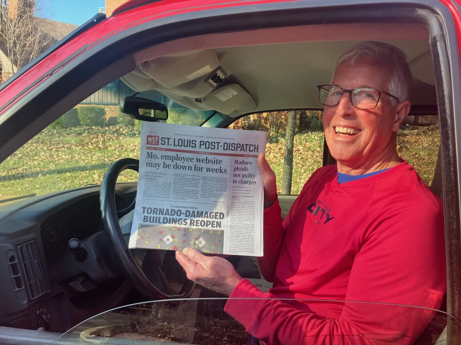 A man in a red van shows off a copy of the St. Louis Post-Dispatch.