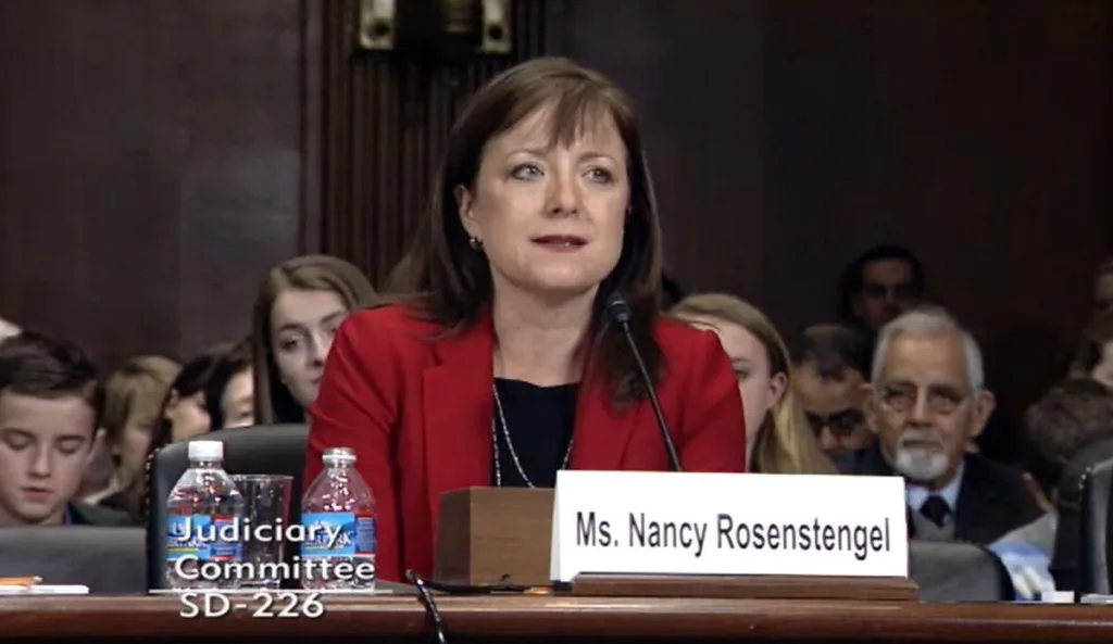 A white woman in a red coat sits at a desk.