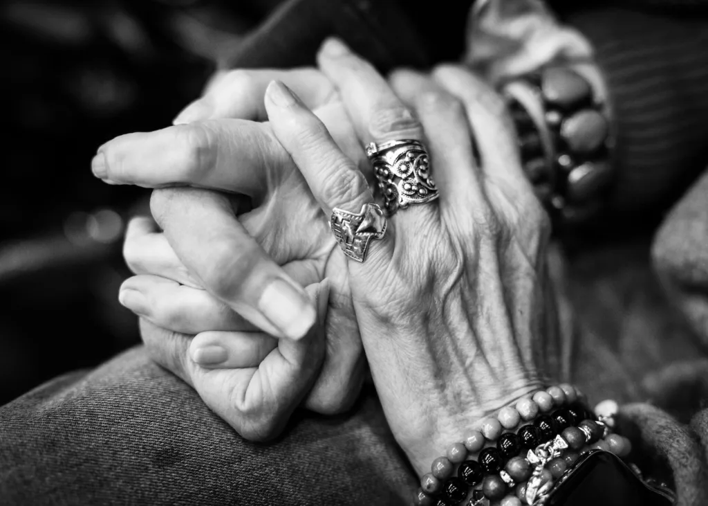 Two hands are entwined with another, laden with rings and bracelets, on top.