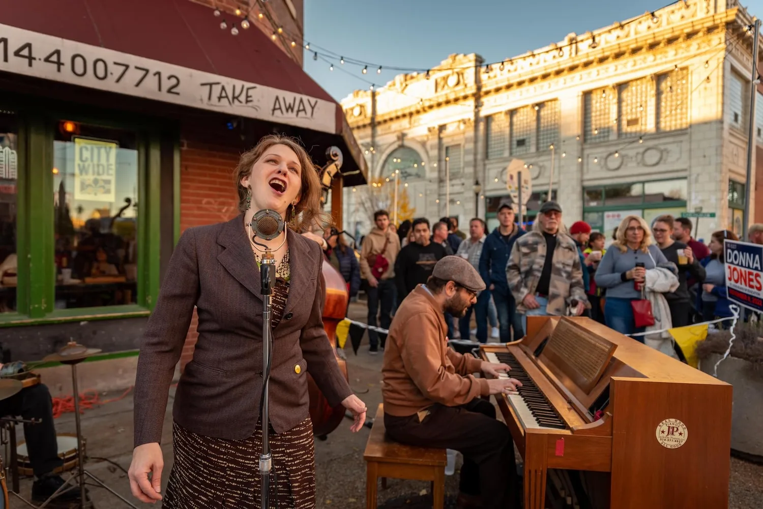 A piano player and singer perform on the street while people watch.