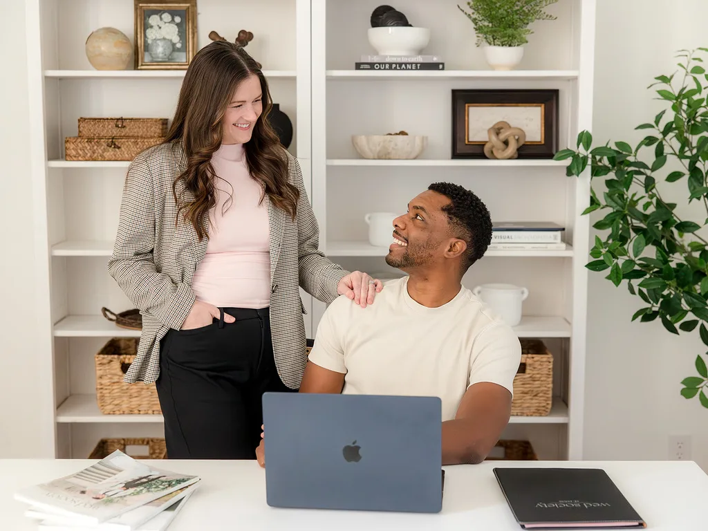 A man sitting at a laptop looks up at a woman.