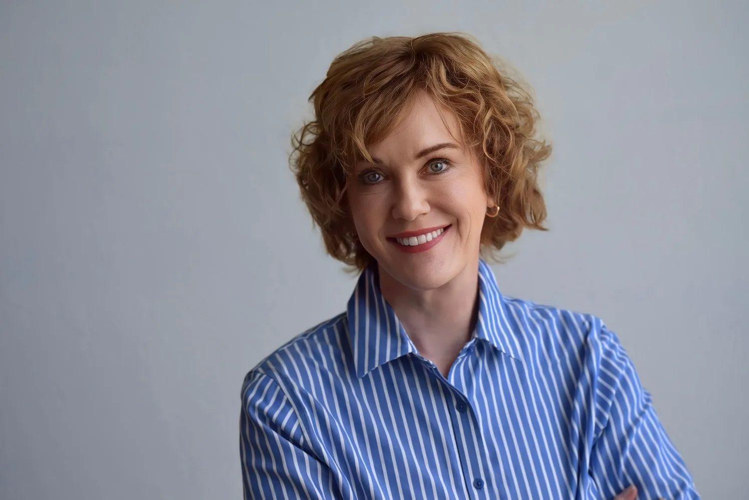 A woman in a blue button-up shirt smiles at the camera.