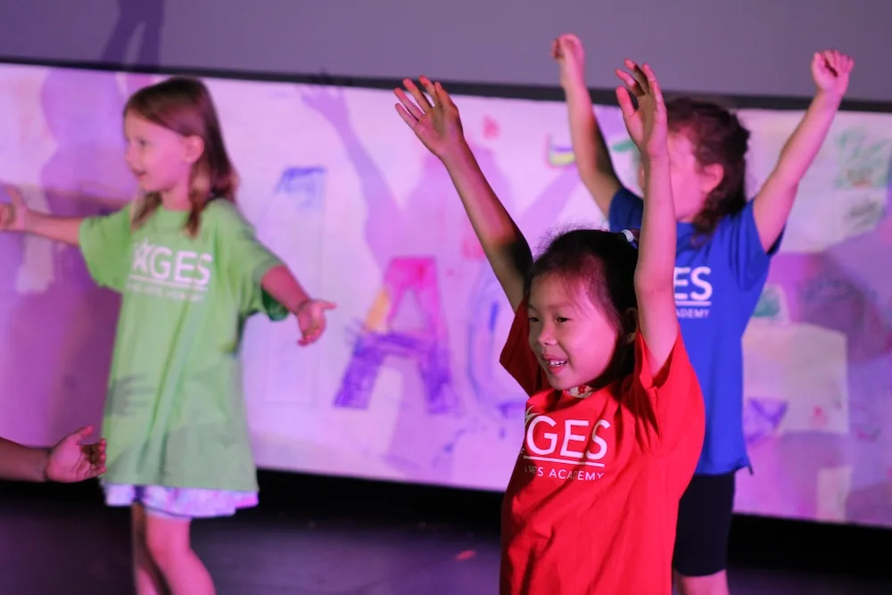 Young students in the STAGES Performing Arts Academy, wearing matching T-shirts, participate in an onstage exercise.