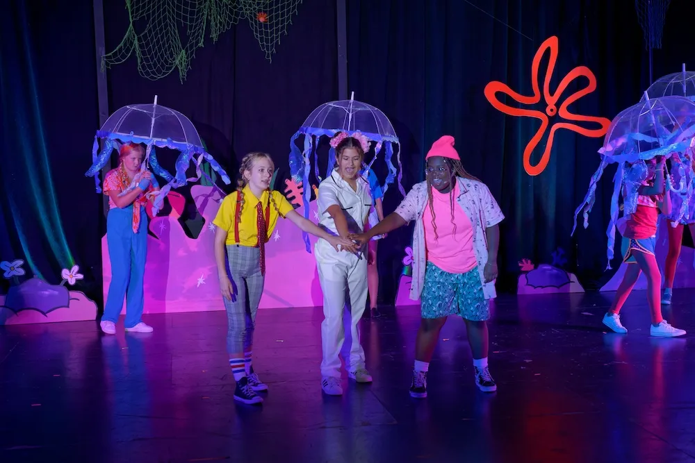 Students perform a colorful under-the-sea scene with jellyfish props during a STAGES Performing Arts Academy production.