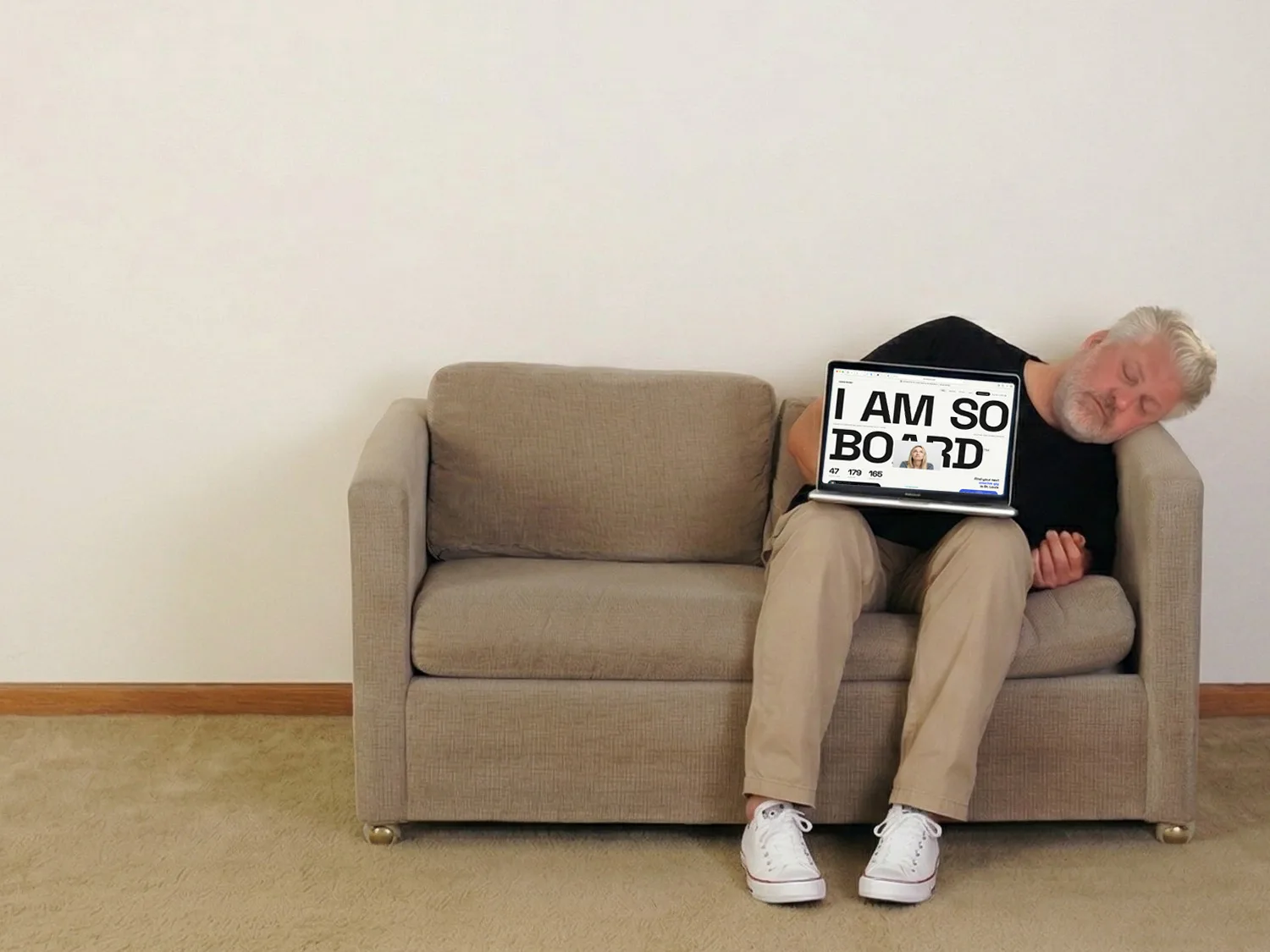 A man snoozes on a couch while holding a laptop displaying a website saying, "I am so board."