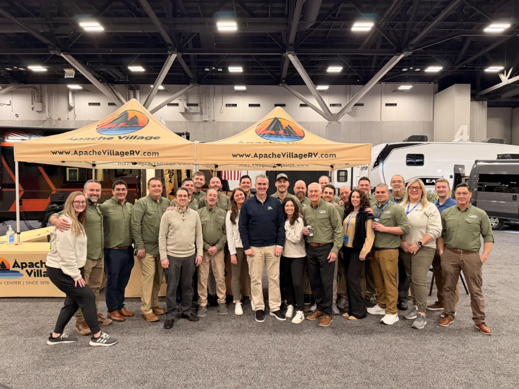 Apache Village RV team members gather at their booth during an industry event.