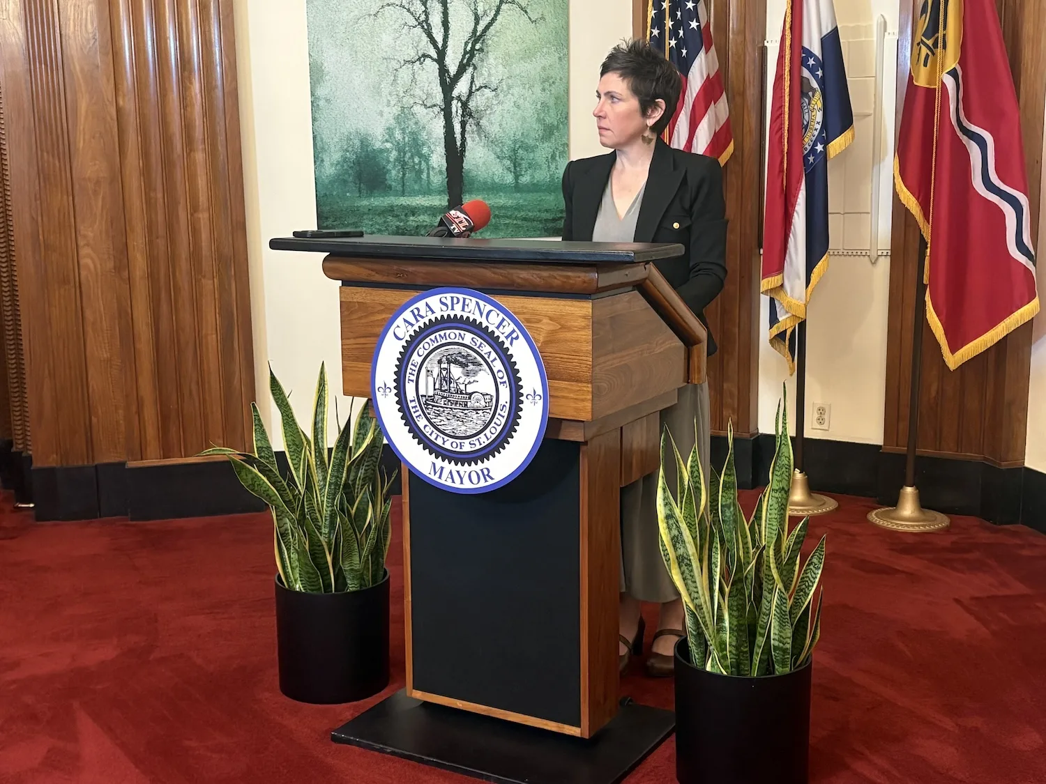 A woman stands at a podium reading "Mayor Cara Spencer."