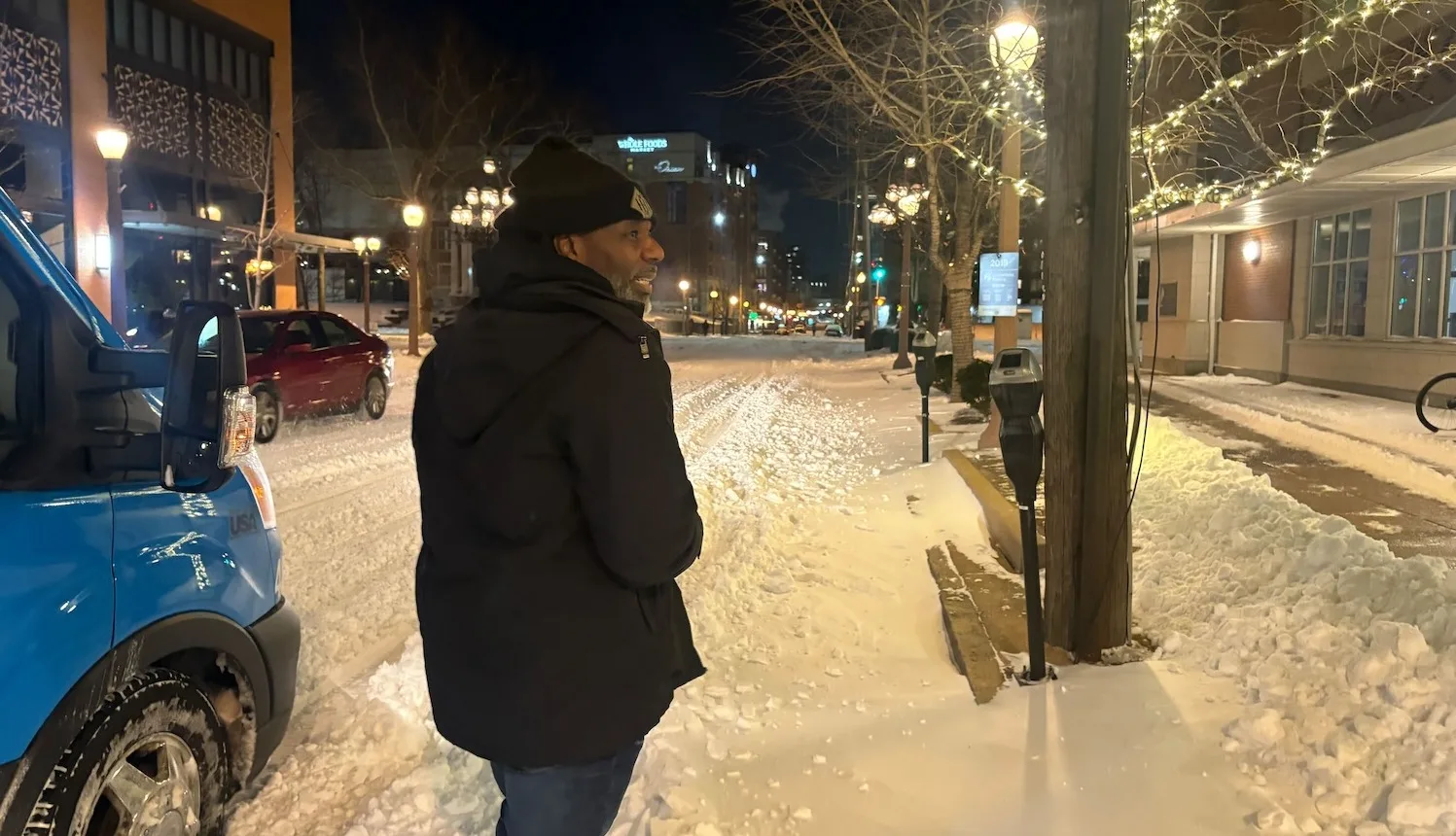 A man walks in the snow next to a city shuttle bus.