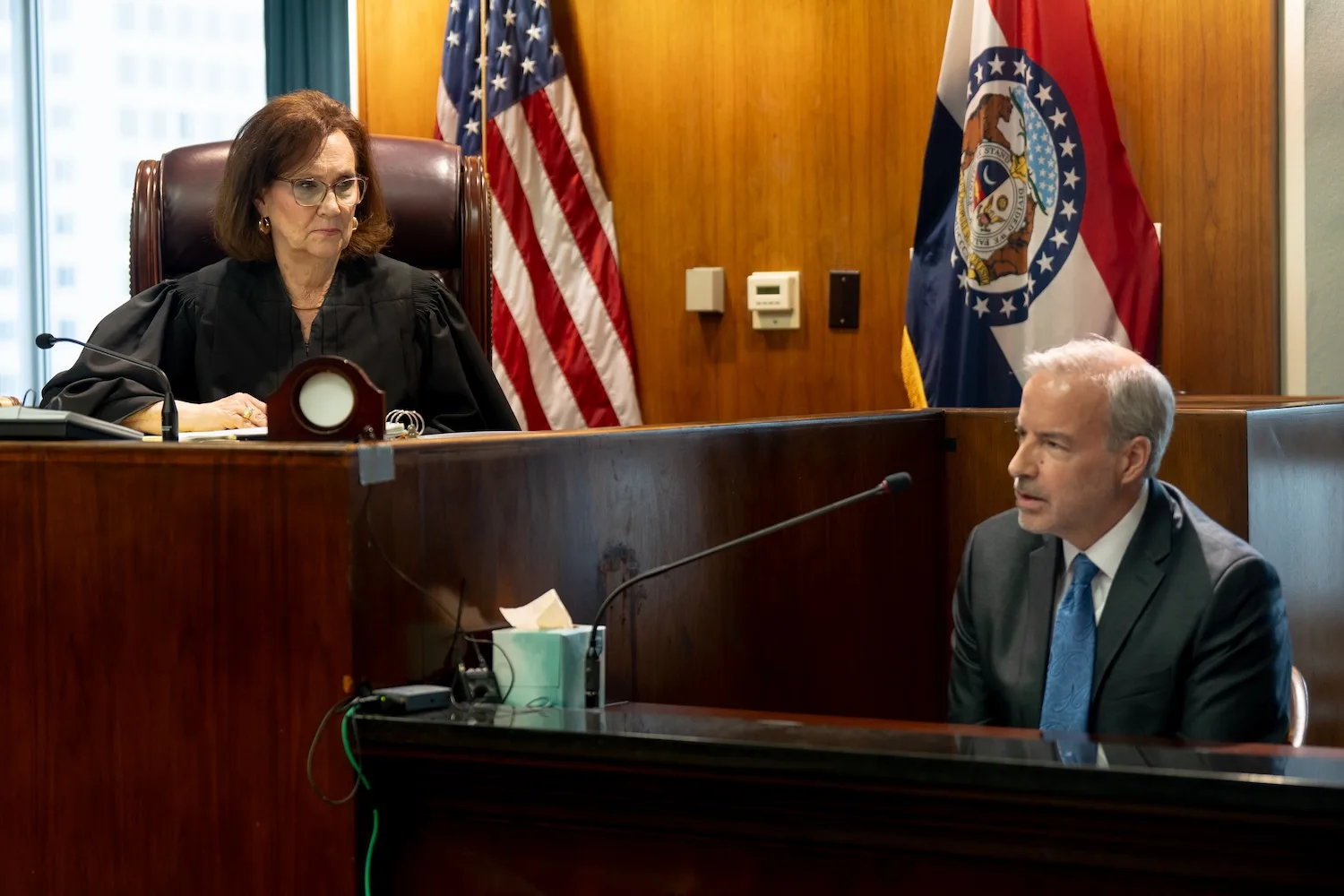 A judge listens to a man in a suit as he testifies in court.