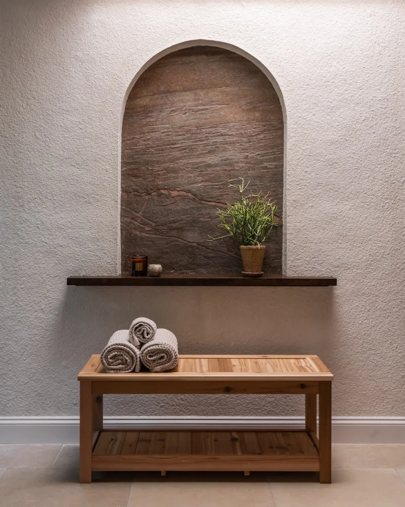 A stone feature wall with an arched niche and spa-like bench serves as the visual centerpiece of the remodeled bathroom.