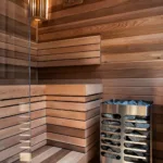Warm wood tones, layered bench seating, and soft lighting give the custom sauna a calming, spa-inspired aesthetic.
