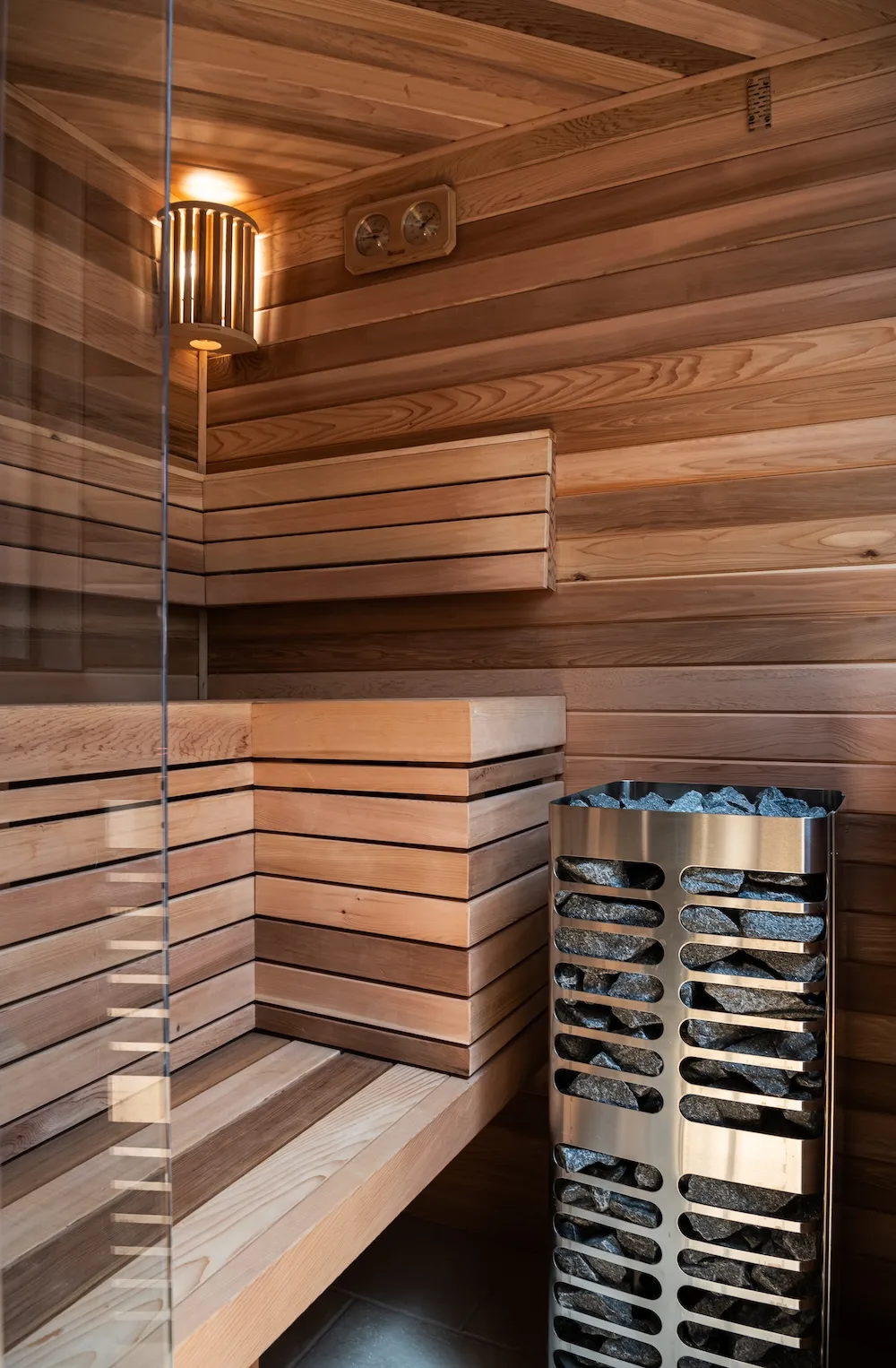 Warm wood tones, layered bench seating, and soft lighting give the custom sauna a calming, spa-inspired aesthetic.