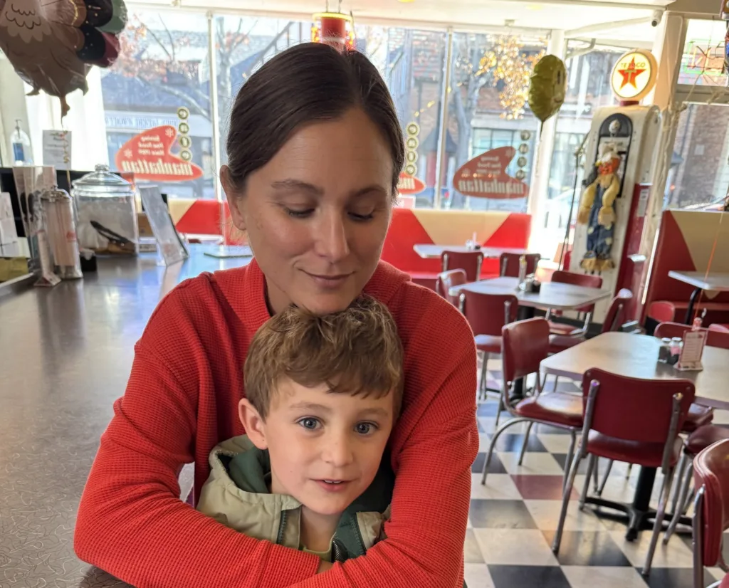 A woman sits with her arms around a small boy at an old-fashioned diner.