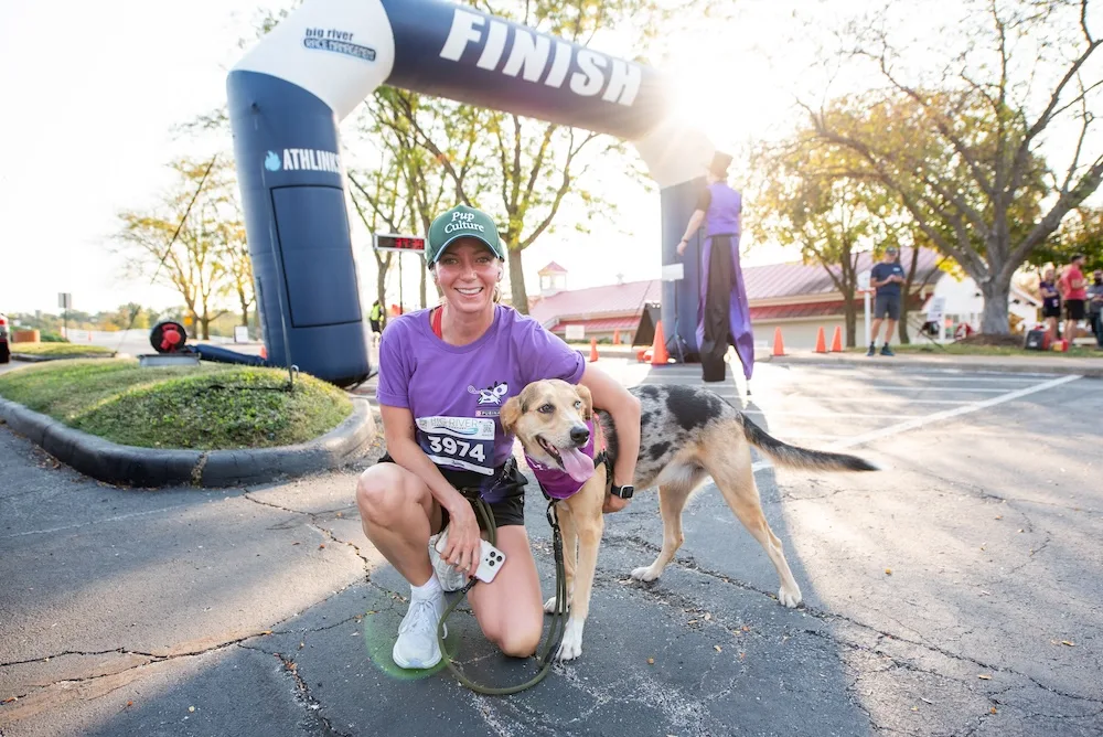 A participant and her dog celebrate after crossing the finish line at a pet-friendly race event.