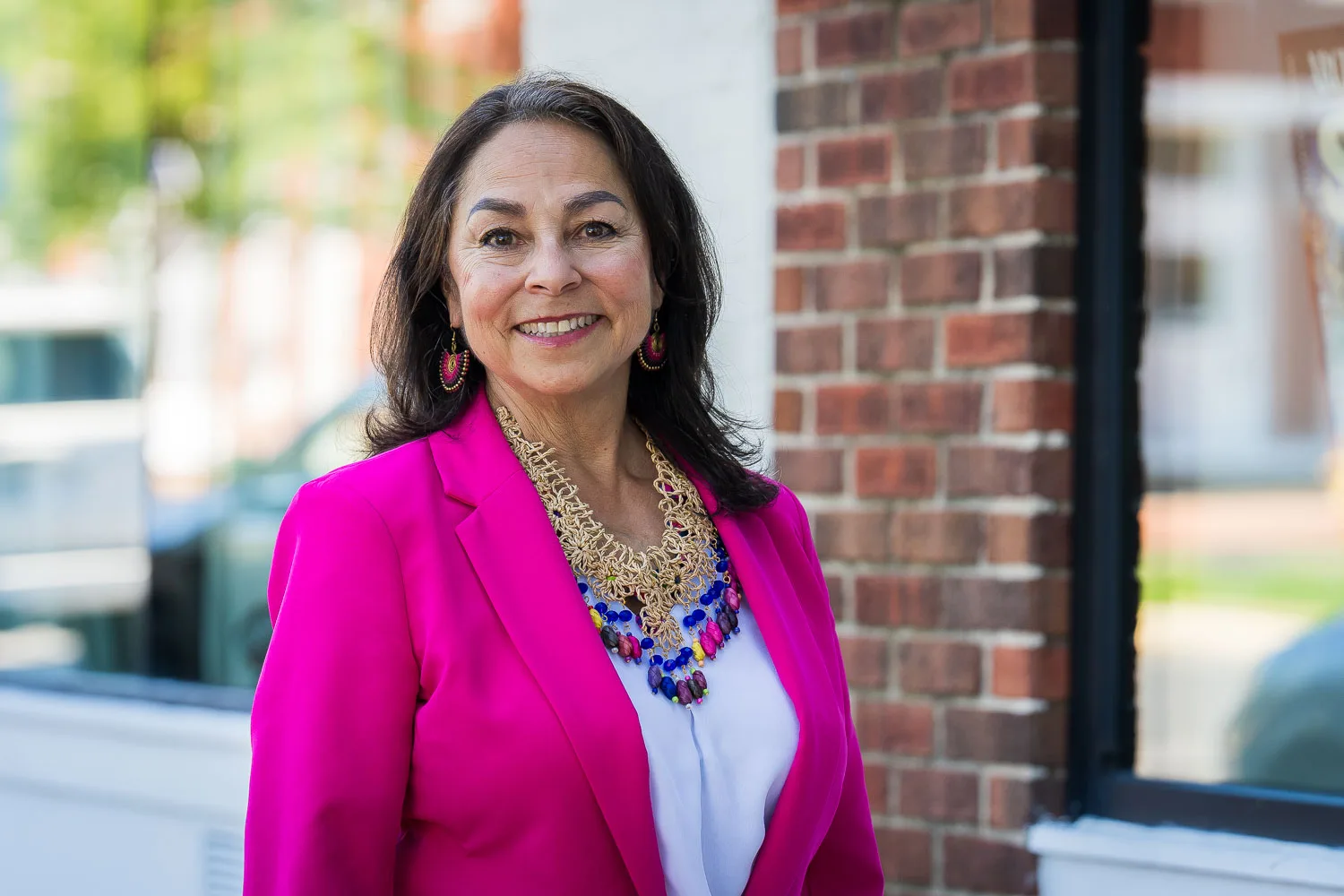 A woman waering a bright pink blazer smiles at the camera.