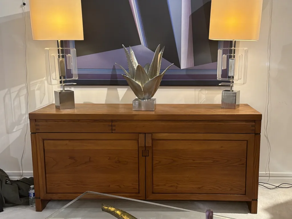 A vintage wooden credenza with two warmly-lit lamps and a metal sculpture of a succulent sitting on top.