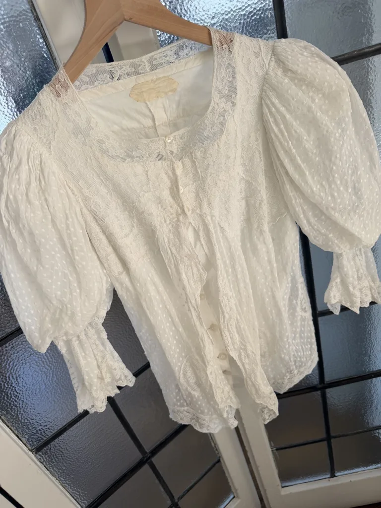A vintage white blouse made of Swiss dot patterned fabric on a hanger.