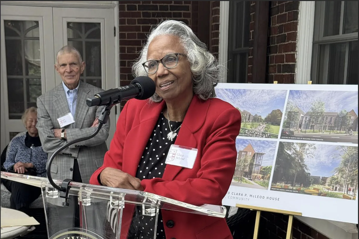 A woman in a red blazer speaks at a podium.