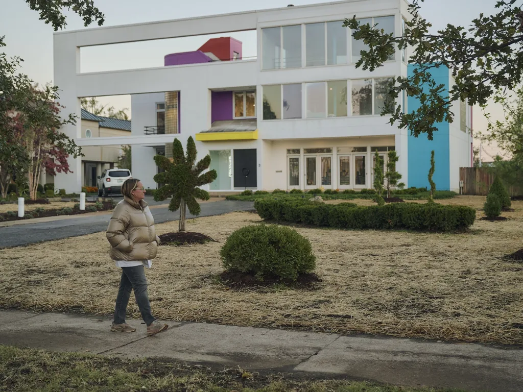 St. Louis artist Katherine Bernhardt walks alongside various shaped topiaries in front of her brightly colored home.