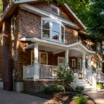 A newly renovated historic home in Webster Groves with warm-toned brick, a large bay window on the second floor and a set of stairs leading to a covered front porch.