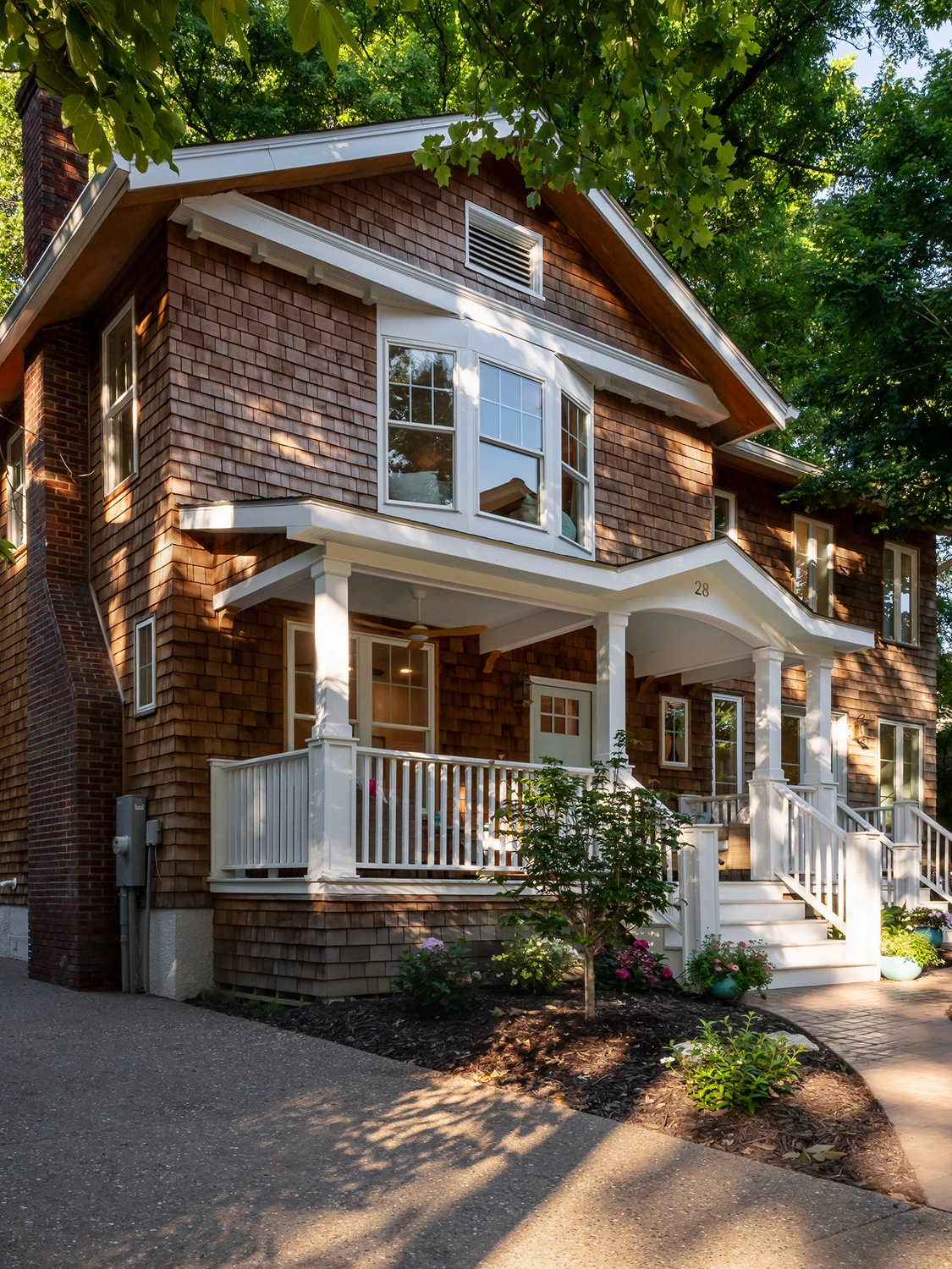 A newly renovated historic home in Webster Groves with warm-toned brick, a large bay window on the second floor and a set of stairs leading to a covered front porch.