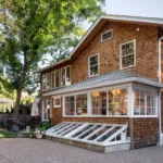 The backyard exterior view of a newly renovated, historic home in Webster Groves with warm-toned brick, several windows and a small patio area.