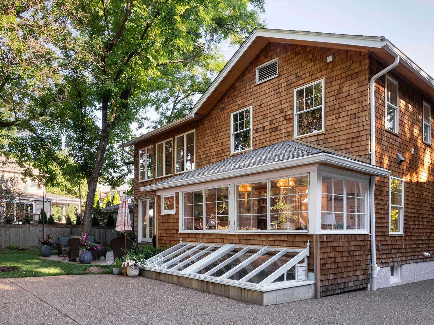 The backyard exterior view of a newly renovated, historic home in Webster Groves with warm-toned brick, several windows and a small patio area.