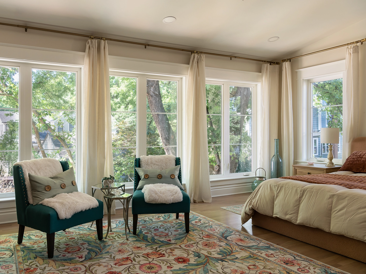 Primary bedroom suite in a newly renovated historic home with almost-floor-to-ceiling windows, a floral area rug, two accent chairs and a bed.