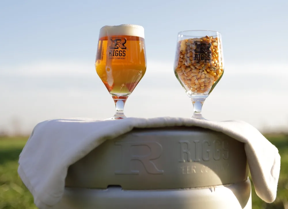 Riggs Beer Company highlights its farm-to-glass approach with beer alongside locally grown corn.