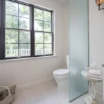 A frosted-glass privacy panel helps visually separate the toilet area without closing it off from the rest of the bathroom.